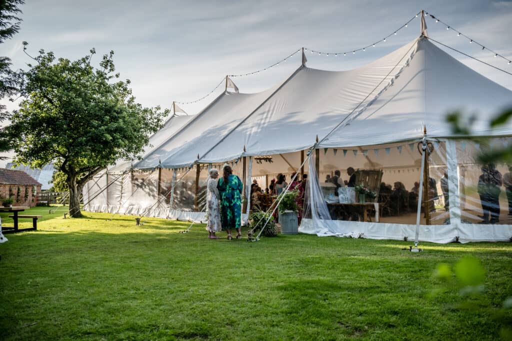 Large white marquee tent set up in a garden with string lights overhead and guests inside.