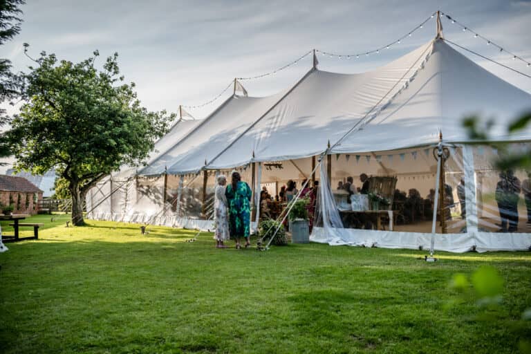 Marquee Wedding Pole MArquee 2026 | Abracadabra Marquees & Events | Abracadabra Marquees & Events Large white marquee tent set up in a garden with string lights overhead and guests inside.