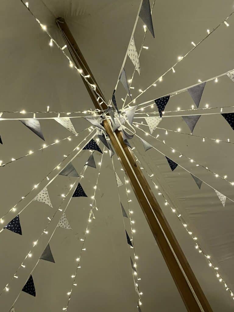 Decorative string lights and blue-and-white pennant banners hanging from a central wooden beam indoors for a festive look for a marquee wedding planning North Yorkshire